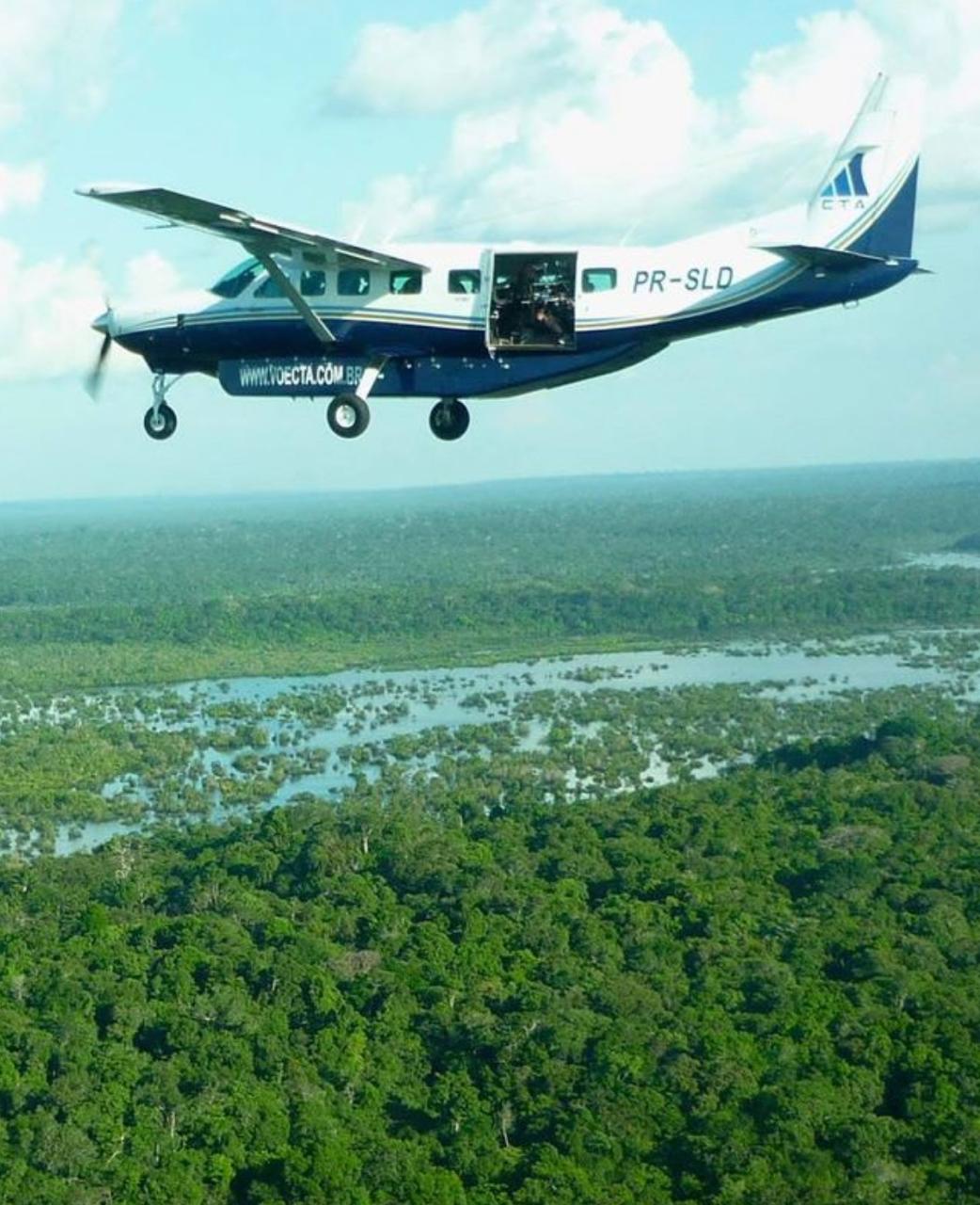 A Brazil Production Services cameraman shoots an aerial view of the jungle with the door of a 9-seater caravan plane open somewhere above the Amazon Rainforest.