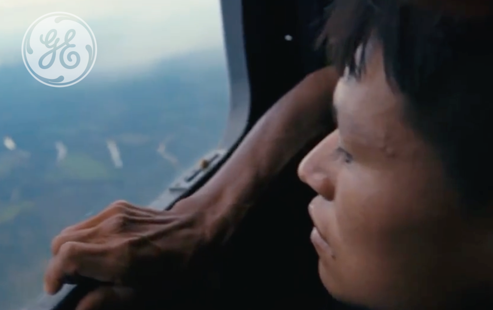 Documentary still with a General Electric logo overlay, showing a person looking out over the Amazon rainforest, from Journey Into Brazil