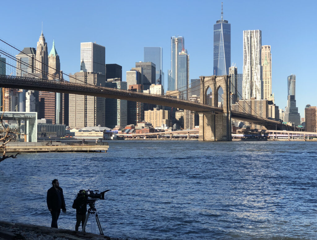 Cameraman filming the Brooklyn Bridge and Lower Manhattan skyline from across the East River